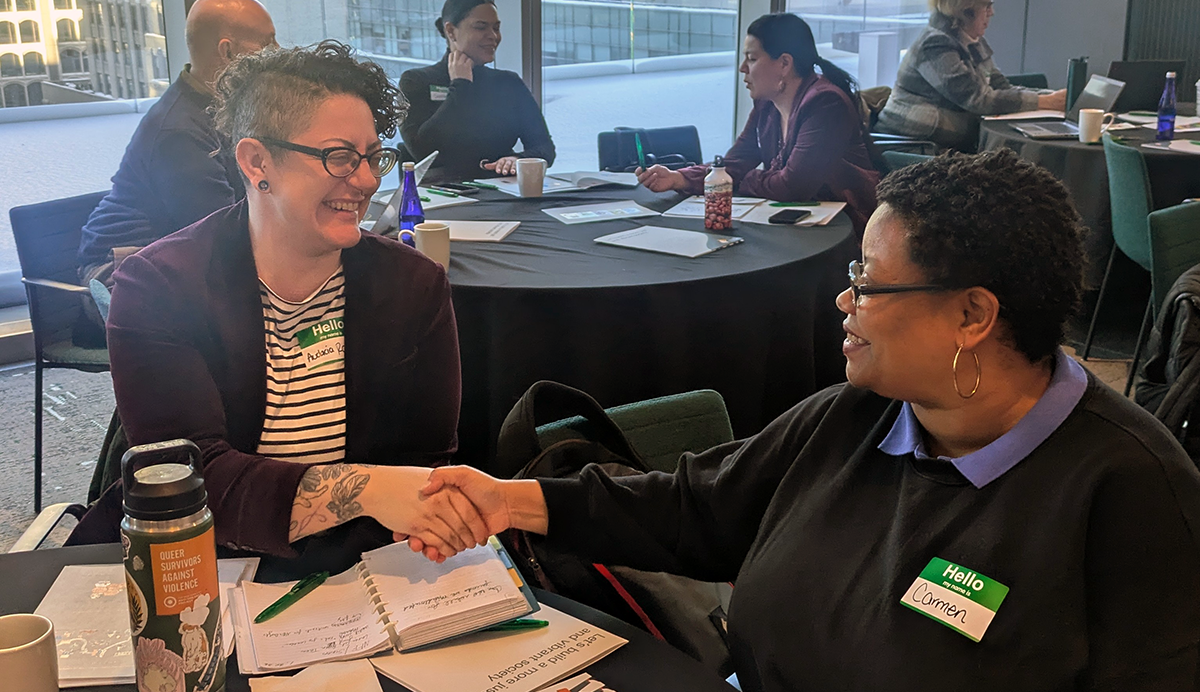 Two women shaking hands sitting at a table