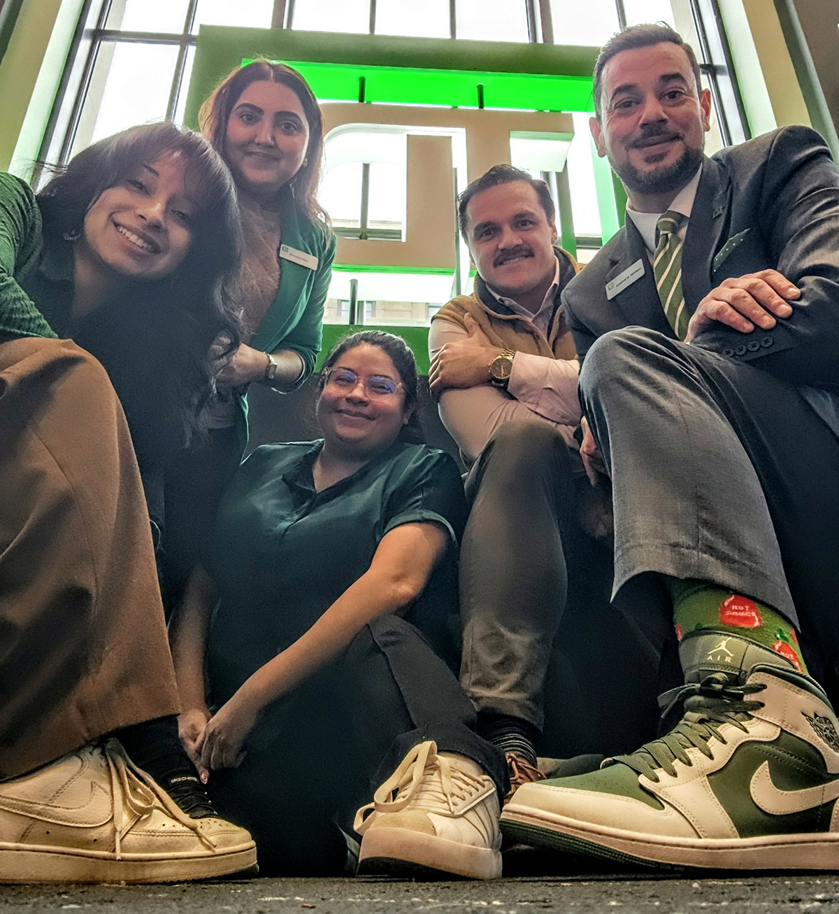 Kristjan smiling with various TD colleagues wearing green sneakers at the Hoboken store
