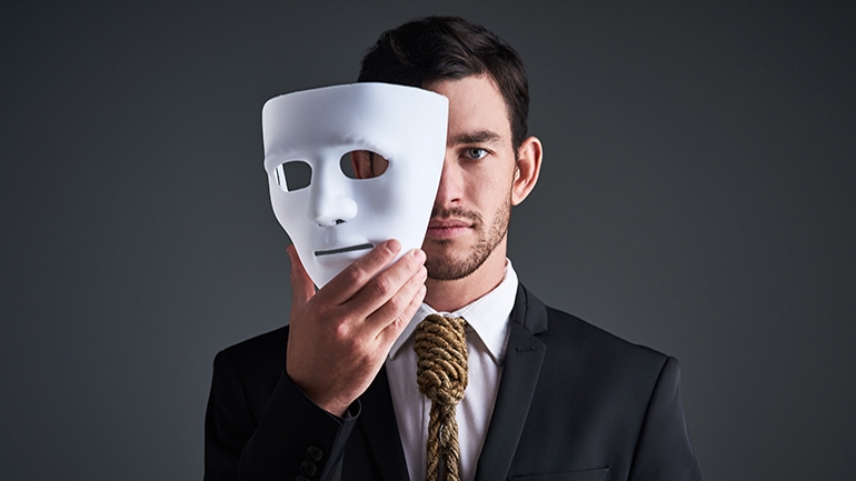 man in suit holding white mask over his face