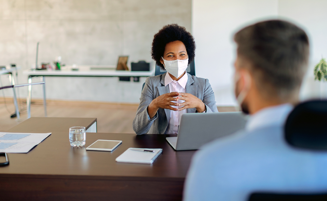 woman with facemask speaking to male coworker