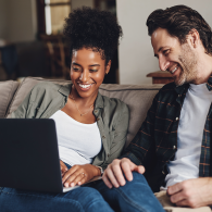 Man and woman sit on couch while doing mortgage research on laptop