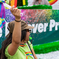 Woman standing and waving a pride flag while wearing a green TD shirt.