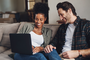 Man and woman sit on couch while doing mortgage research on laptop