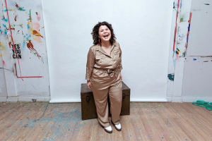 Indigenous artist, Zoey Roys, looking at the camera and laughing while standing in an art studio.