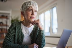 Pensive senior woman working on laptop at home