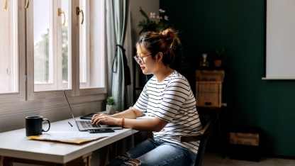 Young casually clothed woman working on laptop at home office stock photo