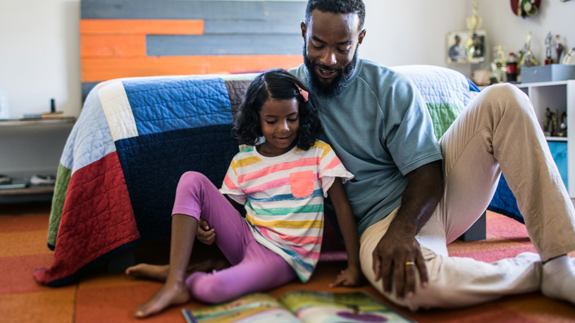 Young African American girl reading a book with her father