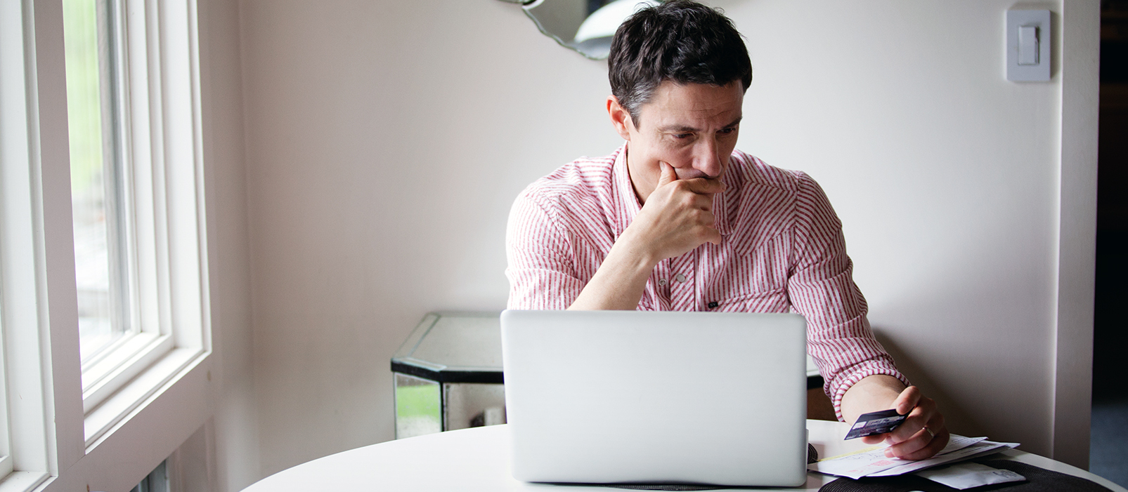 man looking stressed with laptop in front of him and looking at his phone