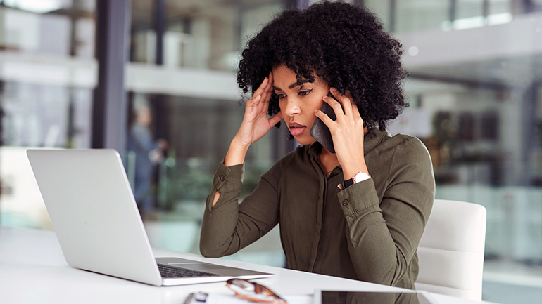 Woman stressed while looking at a laptop and talking on the phone