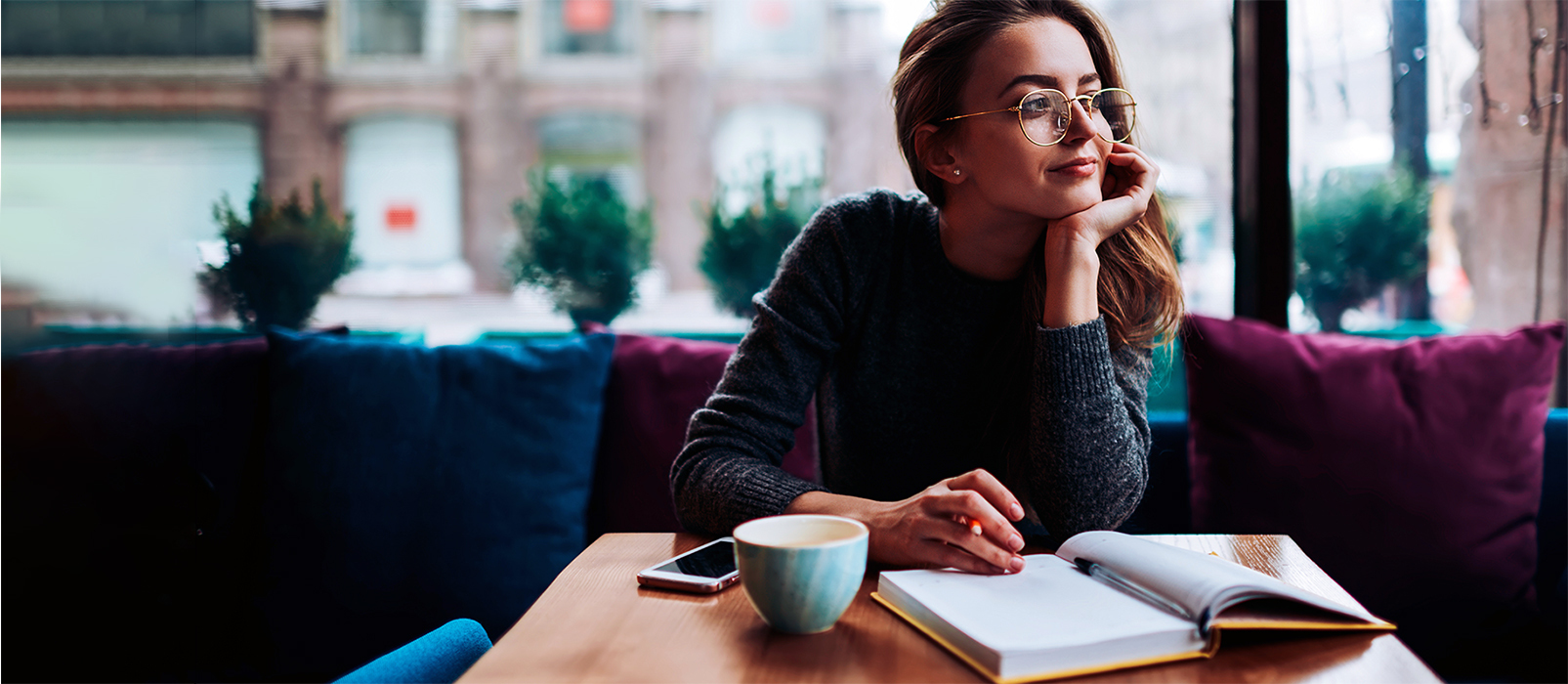 Woman looking thoughtful while writing a list in a notebook in a coffee shop