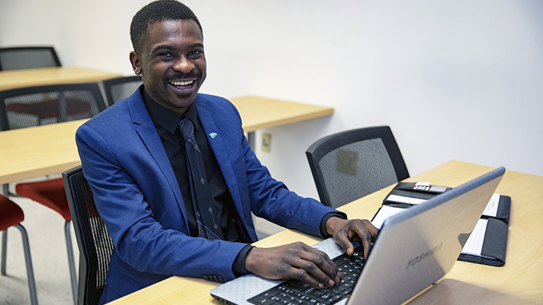 Young, college aged male student smiling while on a computer