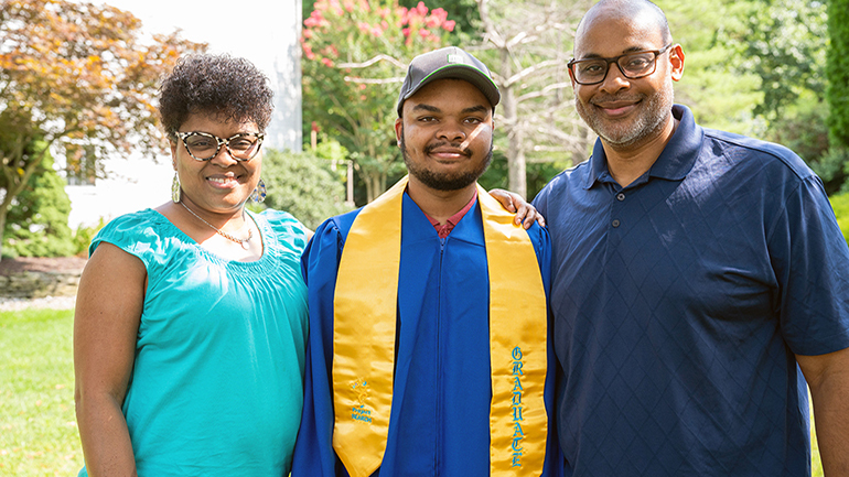 Brandon in his graduation robe with his parents next to him