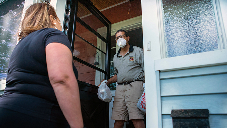 Woman handing goods to someone in a mask at their home