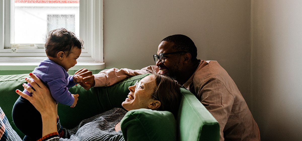 Woman holding a baby on the couch with a man standing behind her