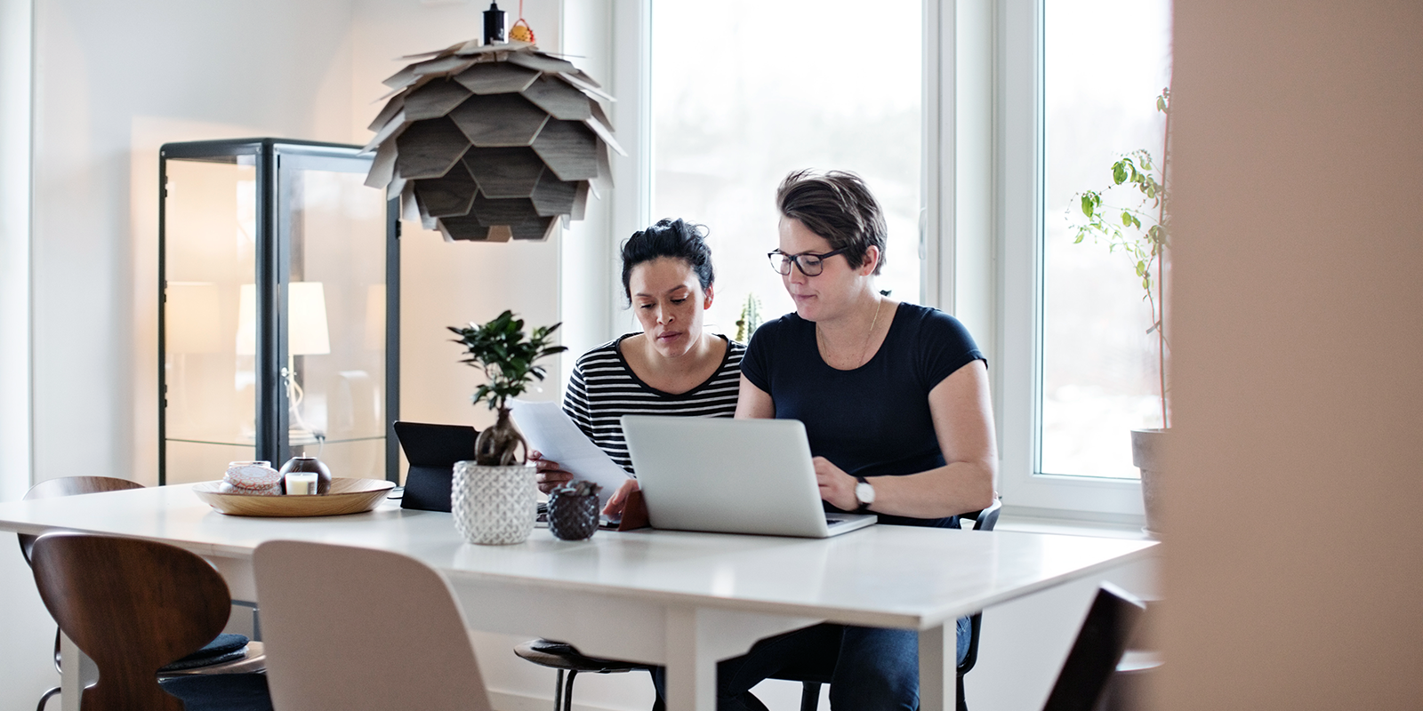 Two women sitting at a kitchen island looking over documents and looking at laptop