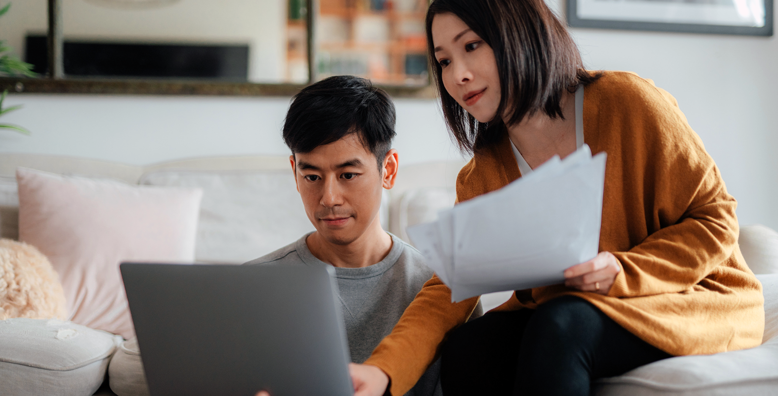 Young woman holding documents while man looks at laptop