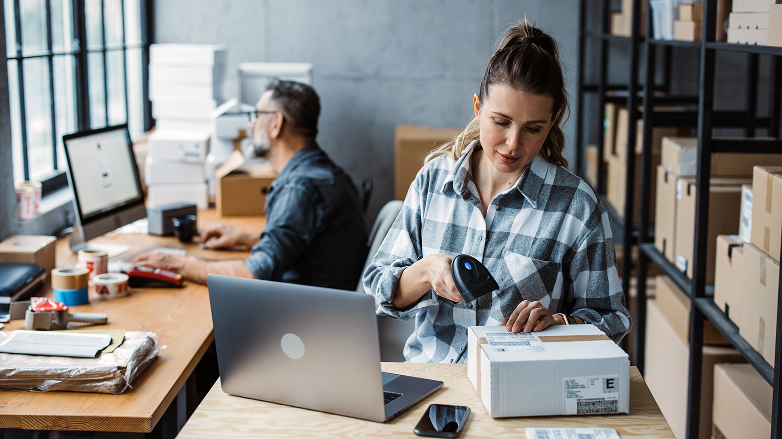 Woman small business owner scanning box and man in the background on a computer