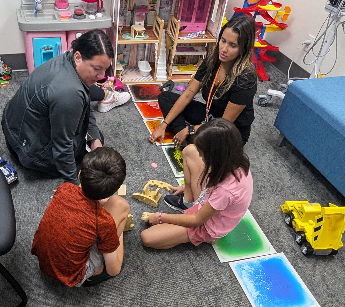 Two women teacher sitting on the floor with a young boy and girl playing with toys