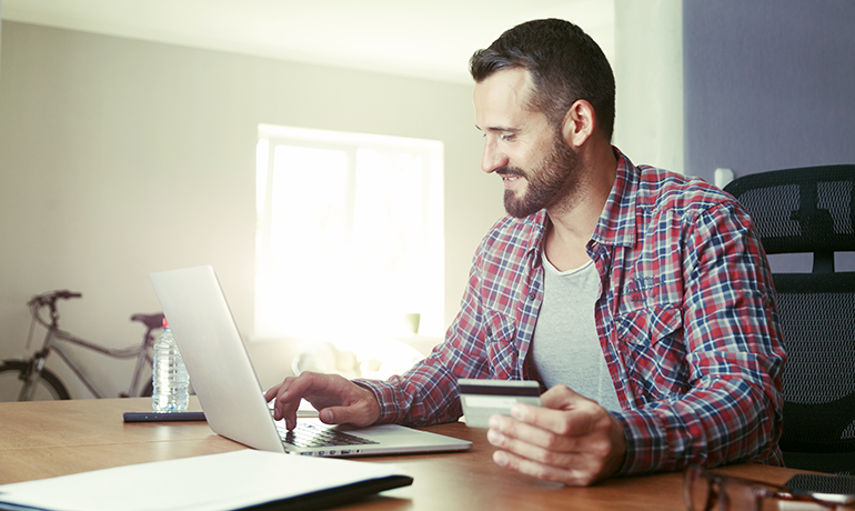 Man on laptop at home with credit card in his hand