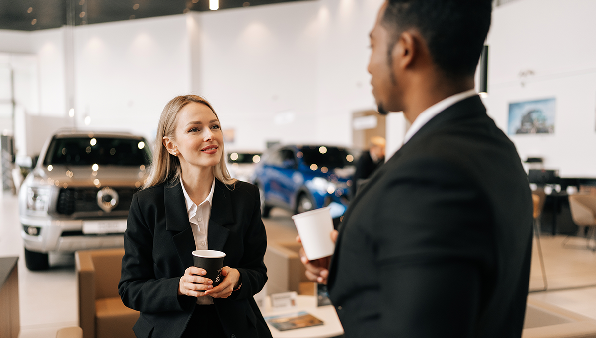 Woman in a car dealership wearing a blazer talking to a man in front of her