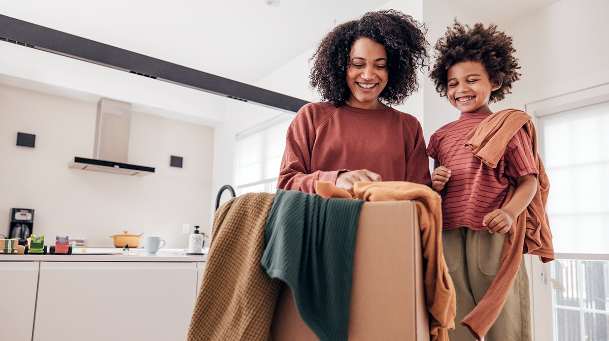 Woman and young boy smiling while looking through a box of clothes at home