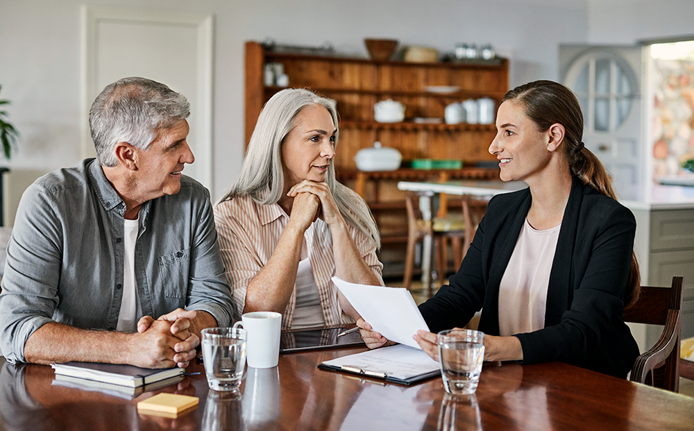 Female financial advisor sitting with older couple at a table discussing paperwork