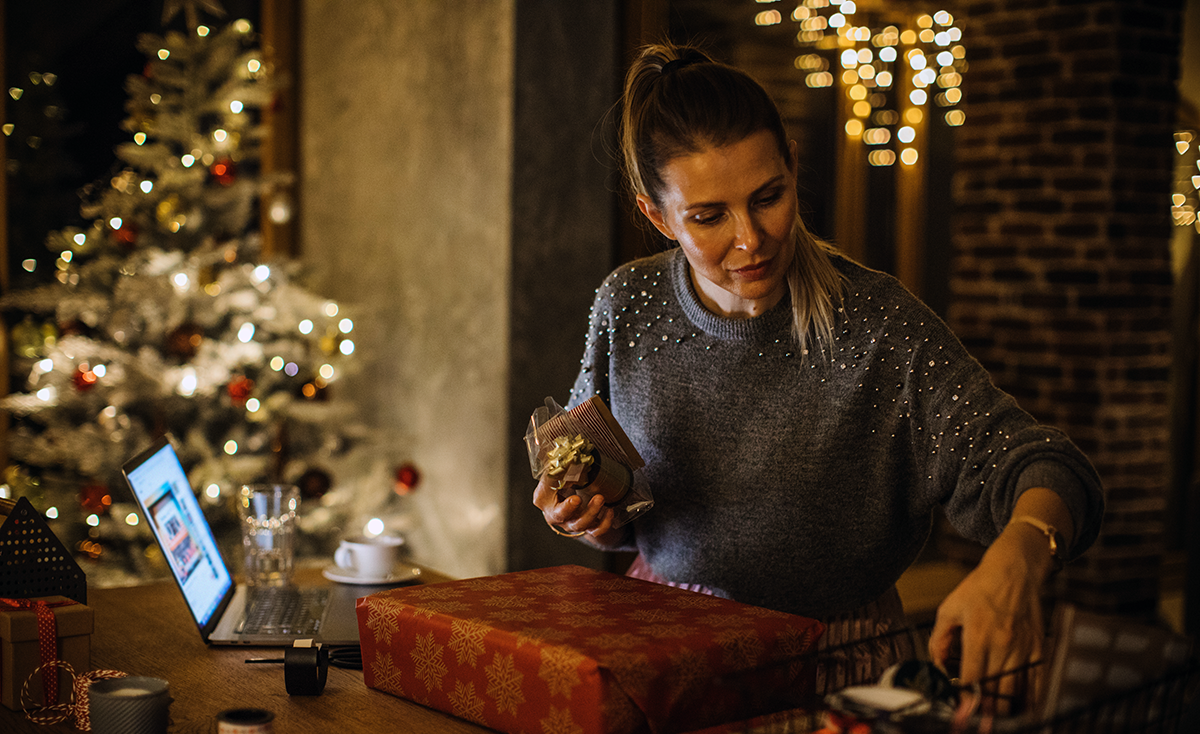 woman at home in a holiday sweat with a christmas tree in the background wrapping presents