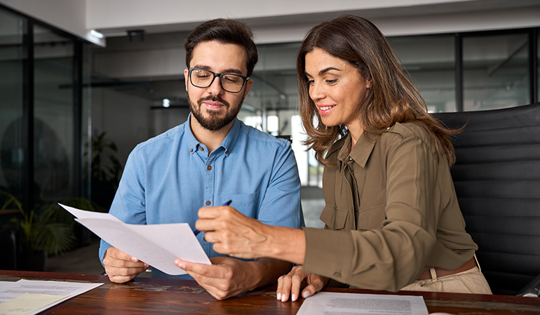 Man with dark hair holding a document while woman with dark next to him points out things with a pen