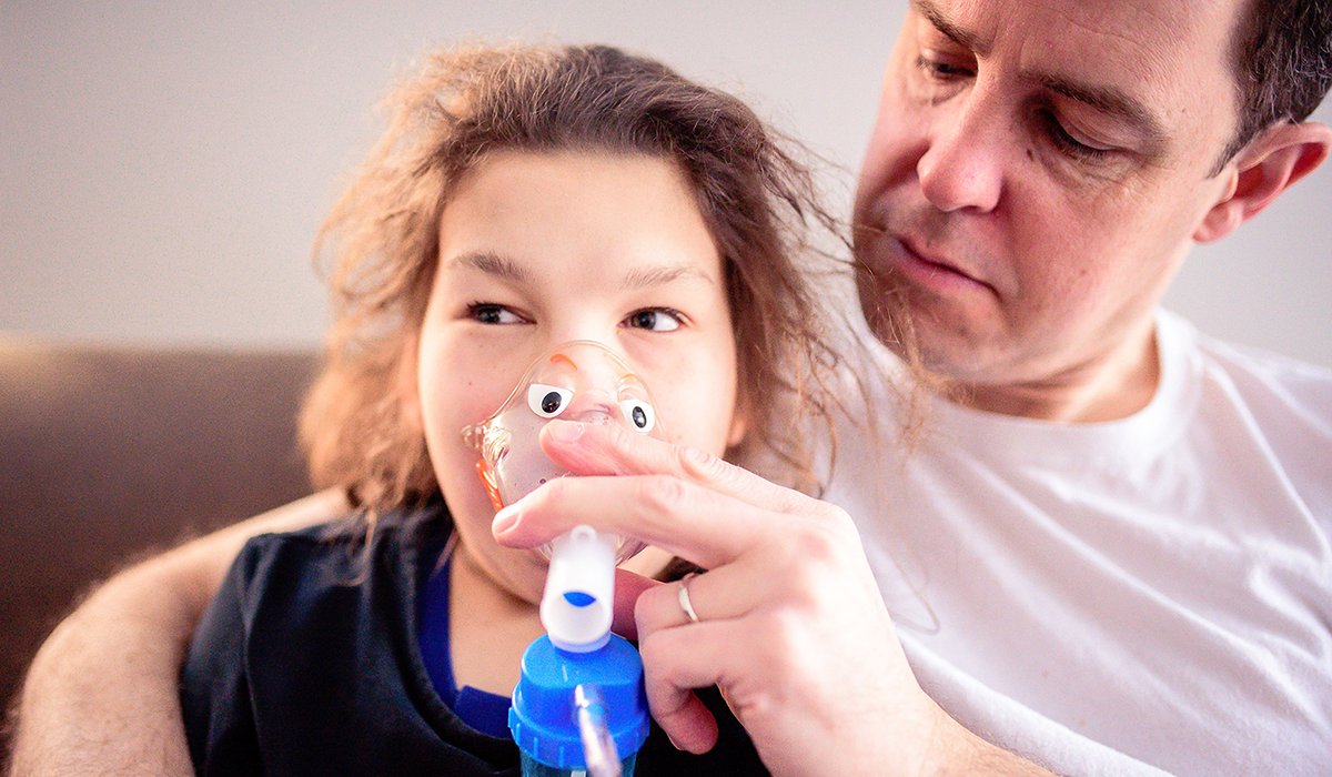 Man helping young girl use an inhaler