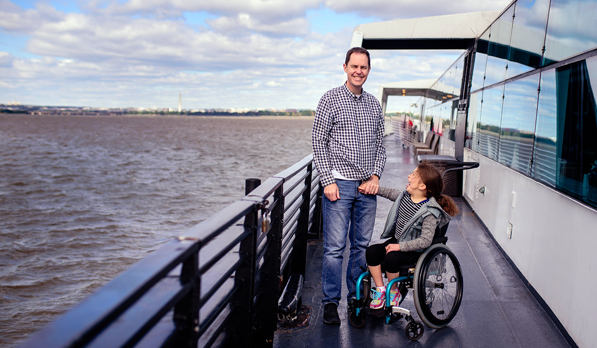 Smiling man and young girl in wheel chair on a boat