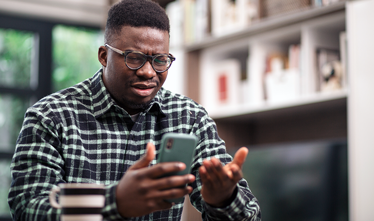 Man at home looking at his phone looking annoyed