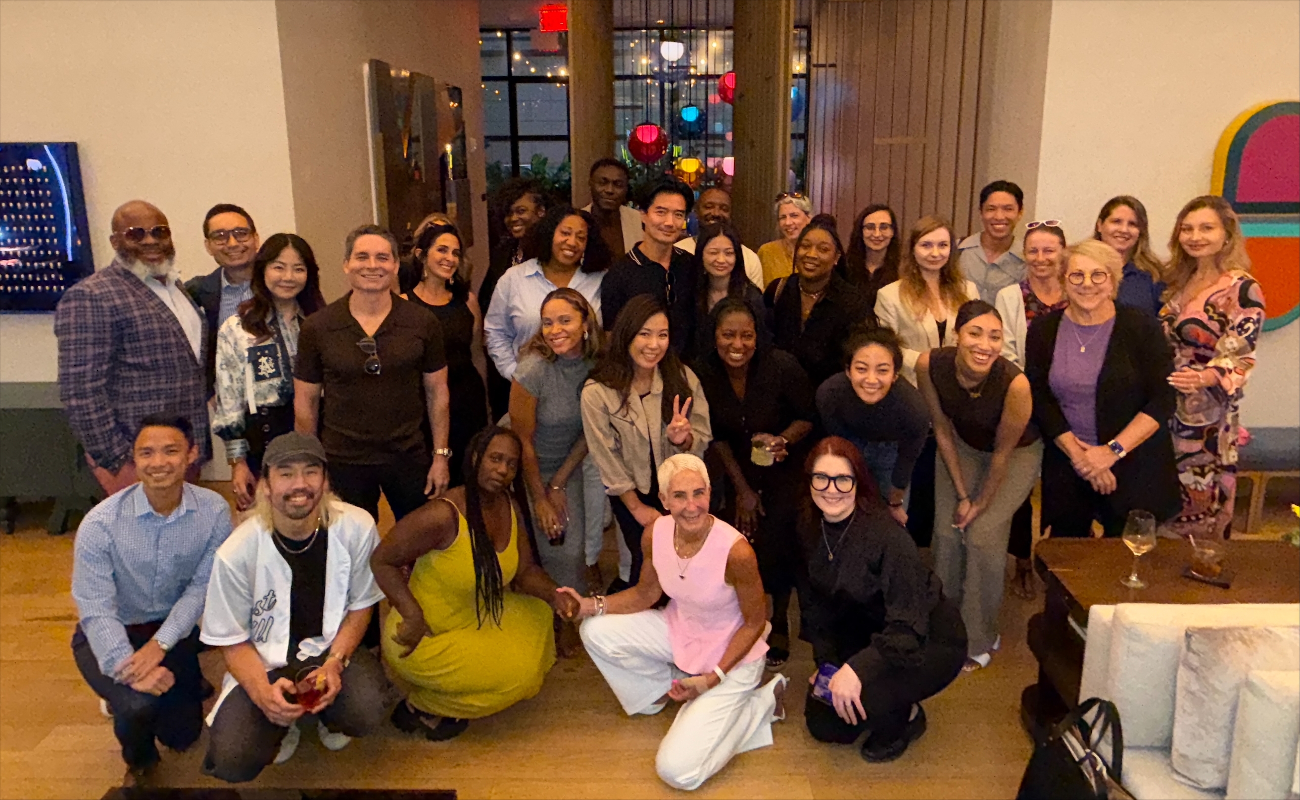Robyn Streisand (center, woman with short white hair, pink sleeveless top and white pants) smiling with a large group of people
