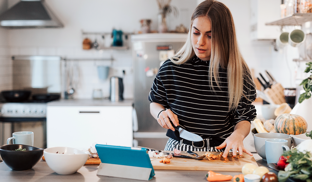 woman watching a tablet in her kitchen while chopping vegetables