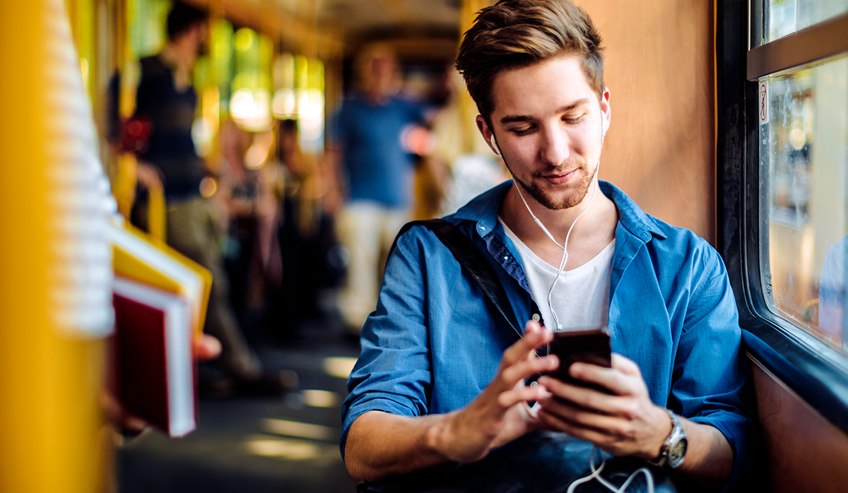 Man on a train wearing wired headphones looking at a phone