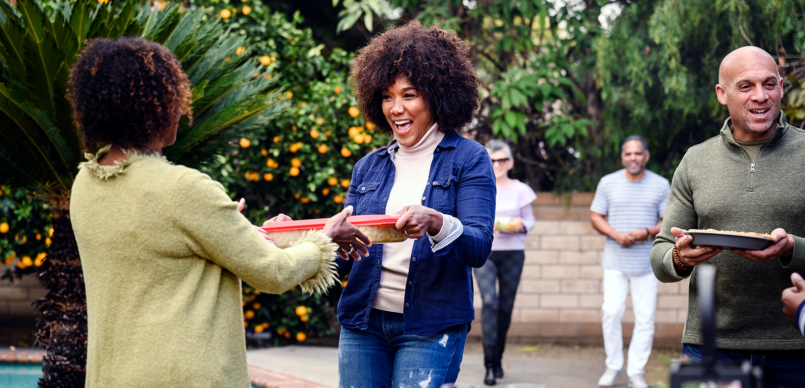 a woman smiling handing over a tupperware container full of food to a family member