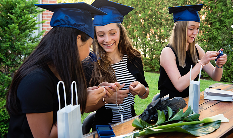 Teenage girls wearing graduation caps with gifts in front of them